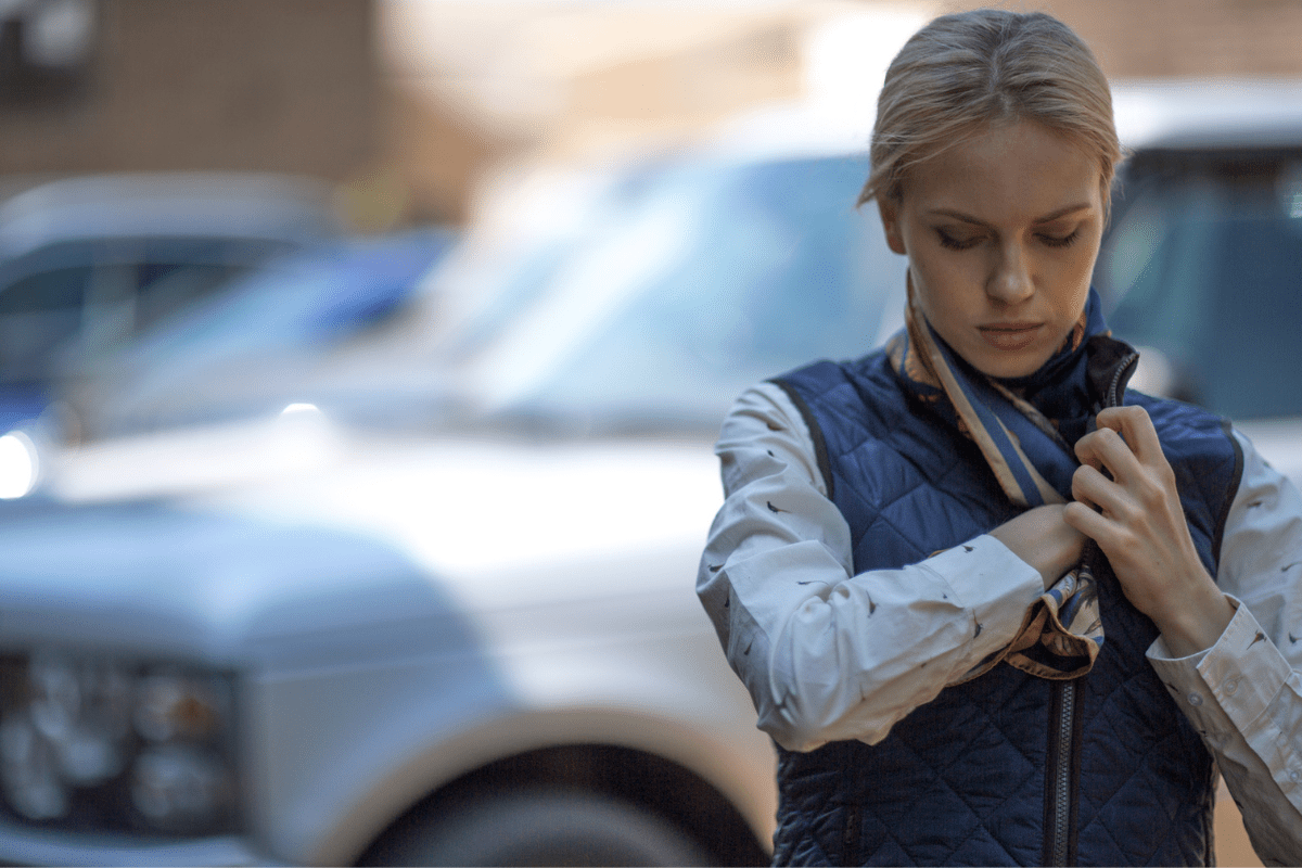 Woman adjusting her jacket in front of a blurred background with vehicles